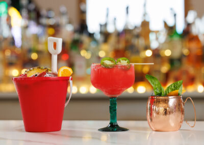 A drink line up at the bar with red bucket, spicy margarita, and Moscow Mule